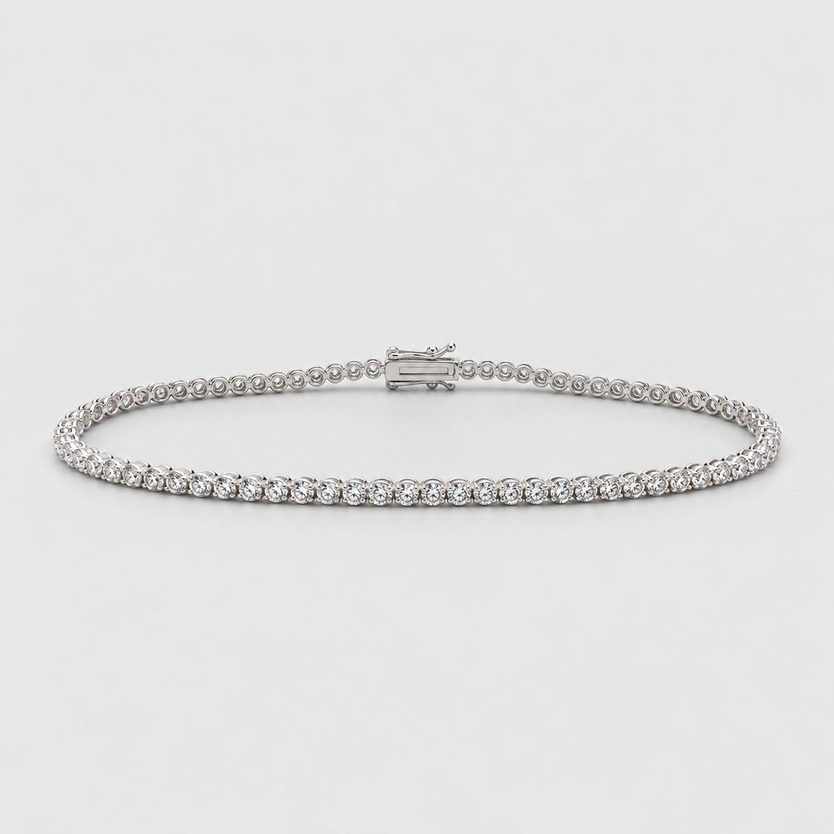 A silver tennis bracelet with a continuous row of small clear gemstones and a clasp closure, photographed on a light gray background.