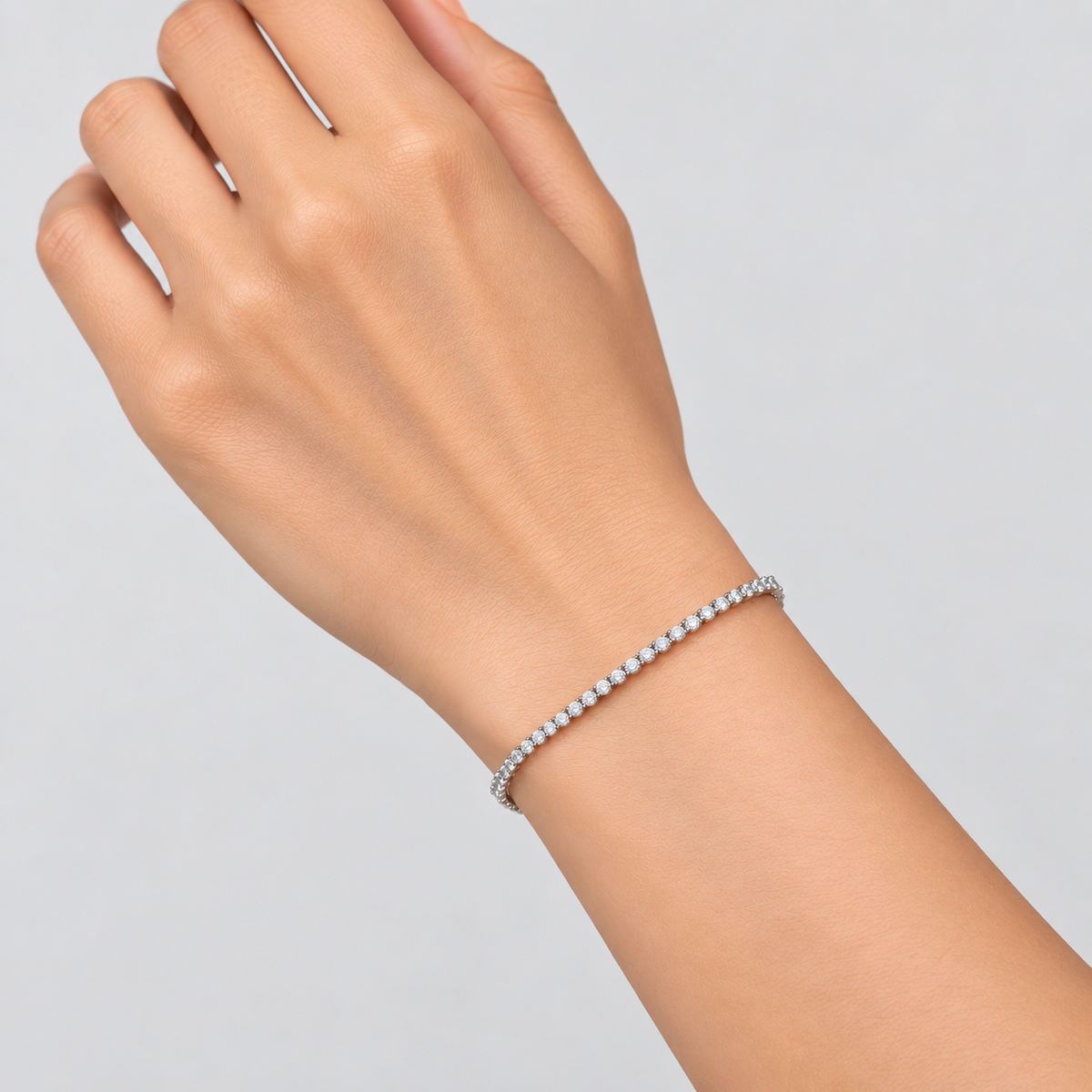 A delicate diamond tennis bracelet on a model's wrist, shown against a clean light gray background.