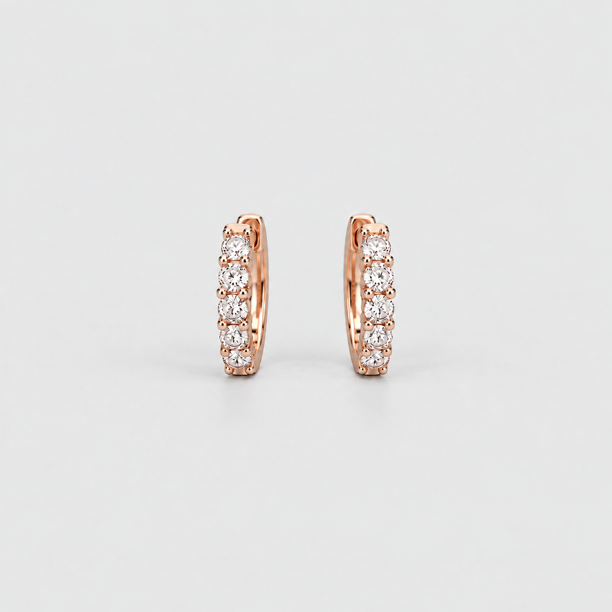 Elegant rose gold huggie hoop earrings with a row of sparkling round lab grown diamonds on a light gray background