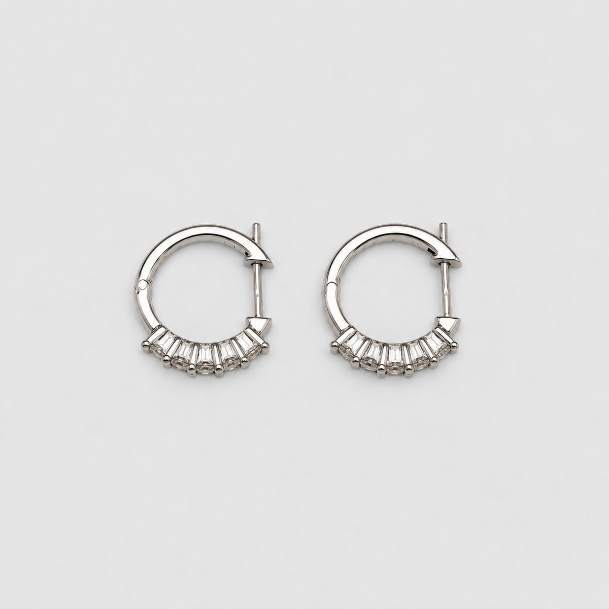 Sparkling white gold hoop earrings with a row of baguette lab grown diamonds on a light gray background