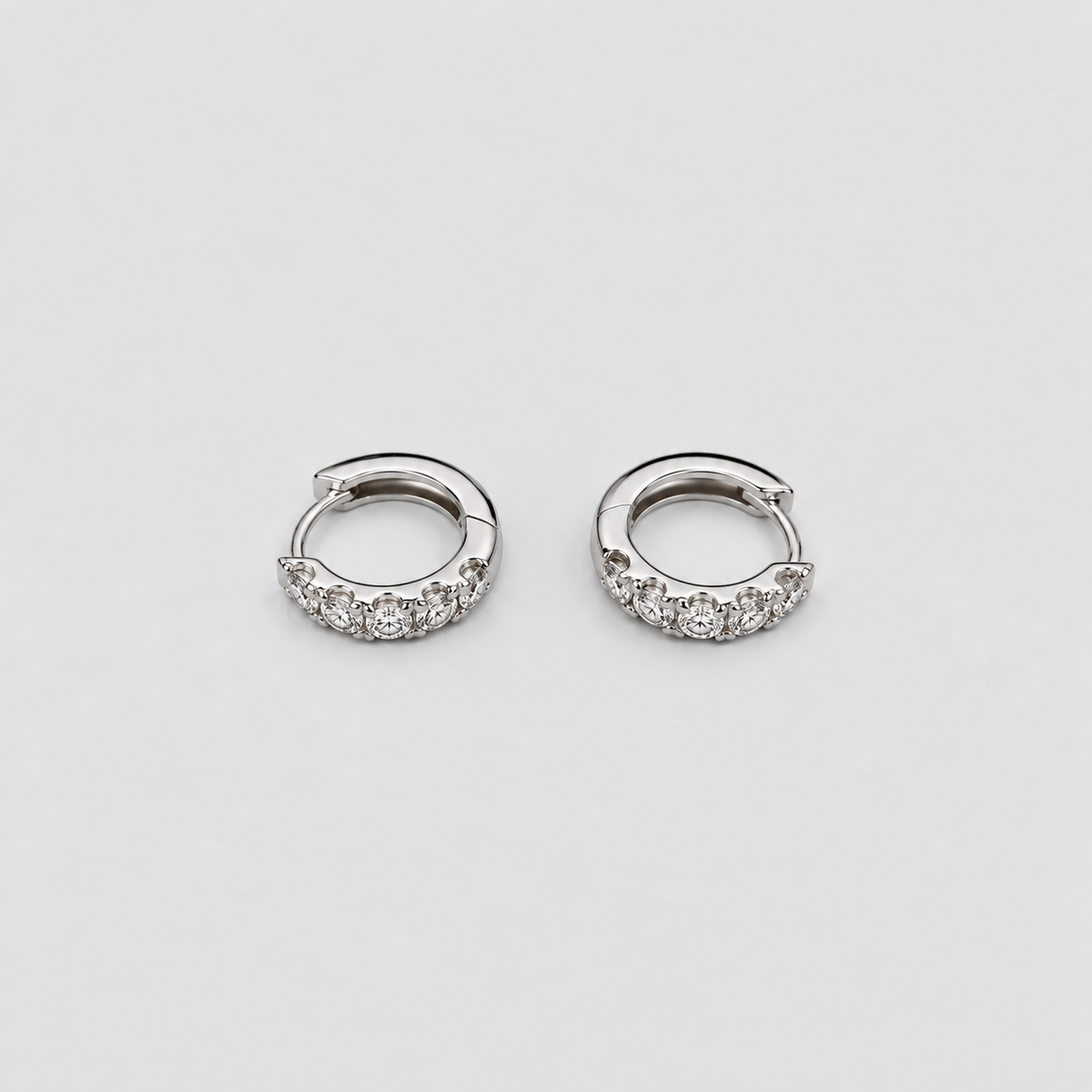 Elegant white gold hoop earrings with a curved row of sparkling round cut lab grown diamonds, flat lay