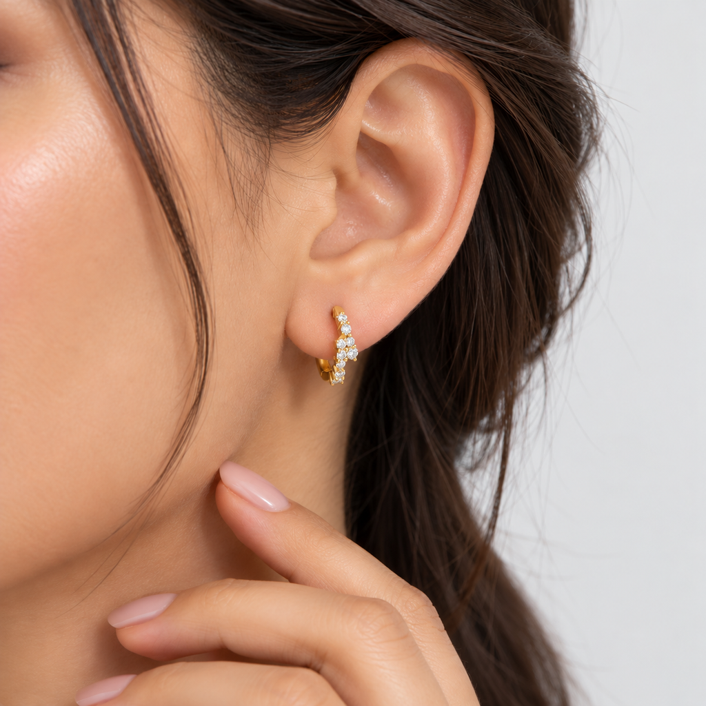 Model wearing yellow gold cluster huggie earrings with round cut lab grown diamonds, hand resting near neck