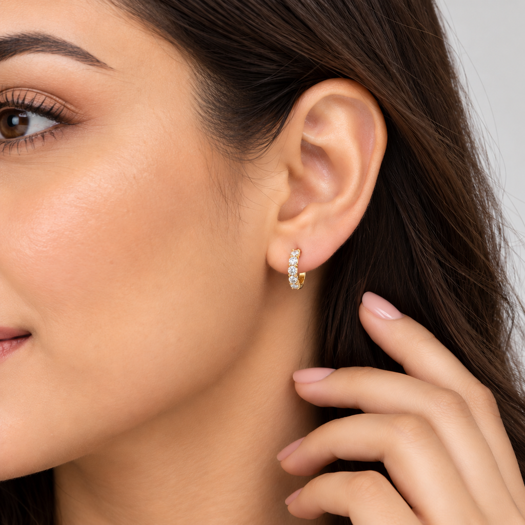Woman wearing 14K yellow gold lab grown diamond huggie hoop earrings with round cut diamonds, close-up side view