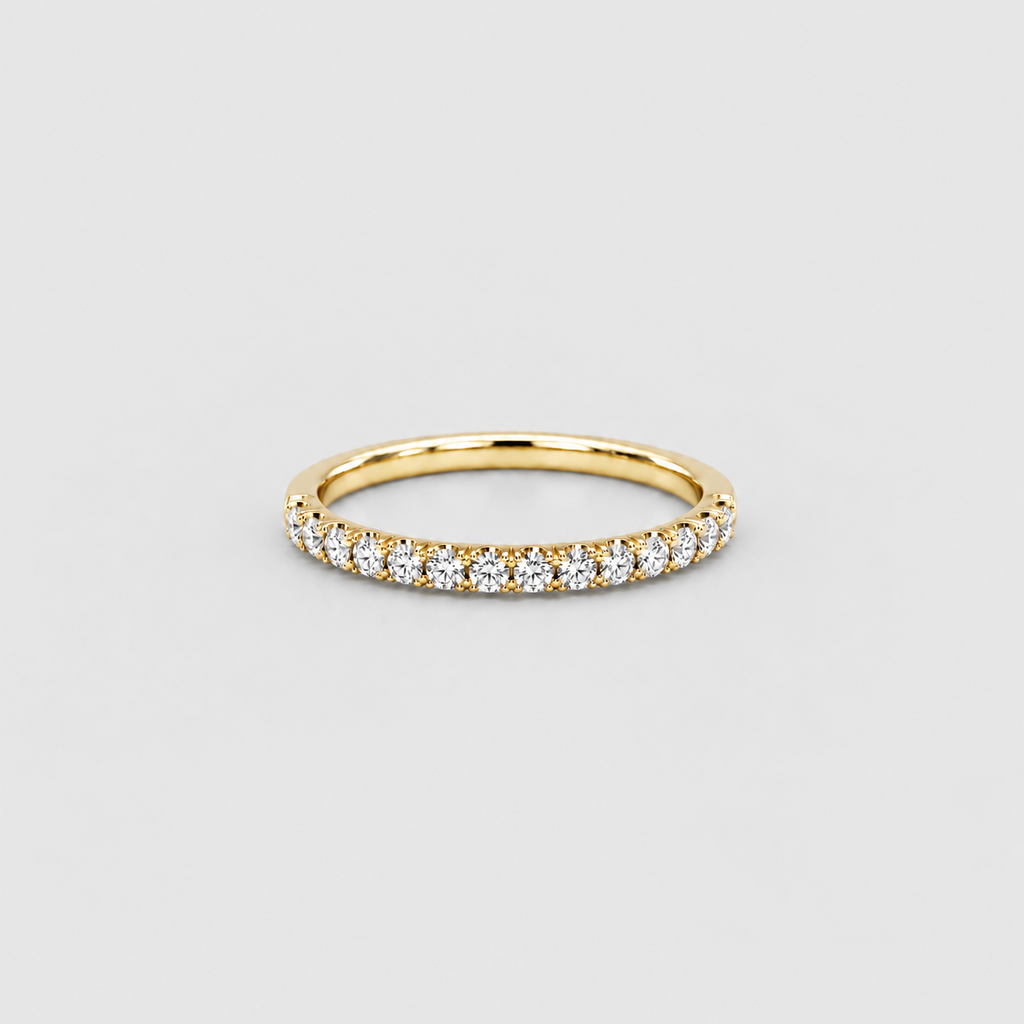 A yellow gold eternity ring set with a row of round-cut clear gemstones, photographed on a neutral light gray background.