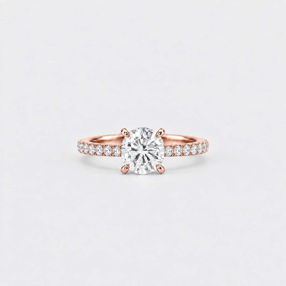 A rose gold solitaire engagement ring with a round-cut center diamond and pavé-set diamonds along the shoulders, centered on a light gray background.
