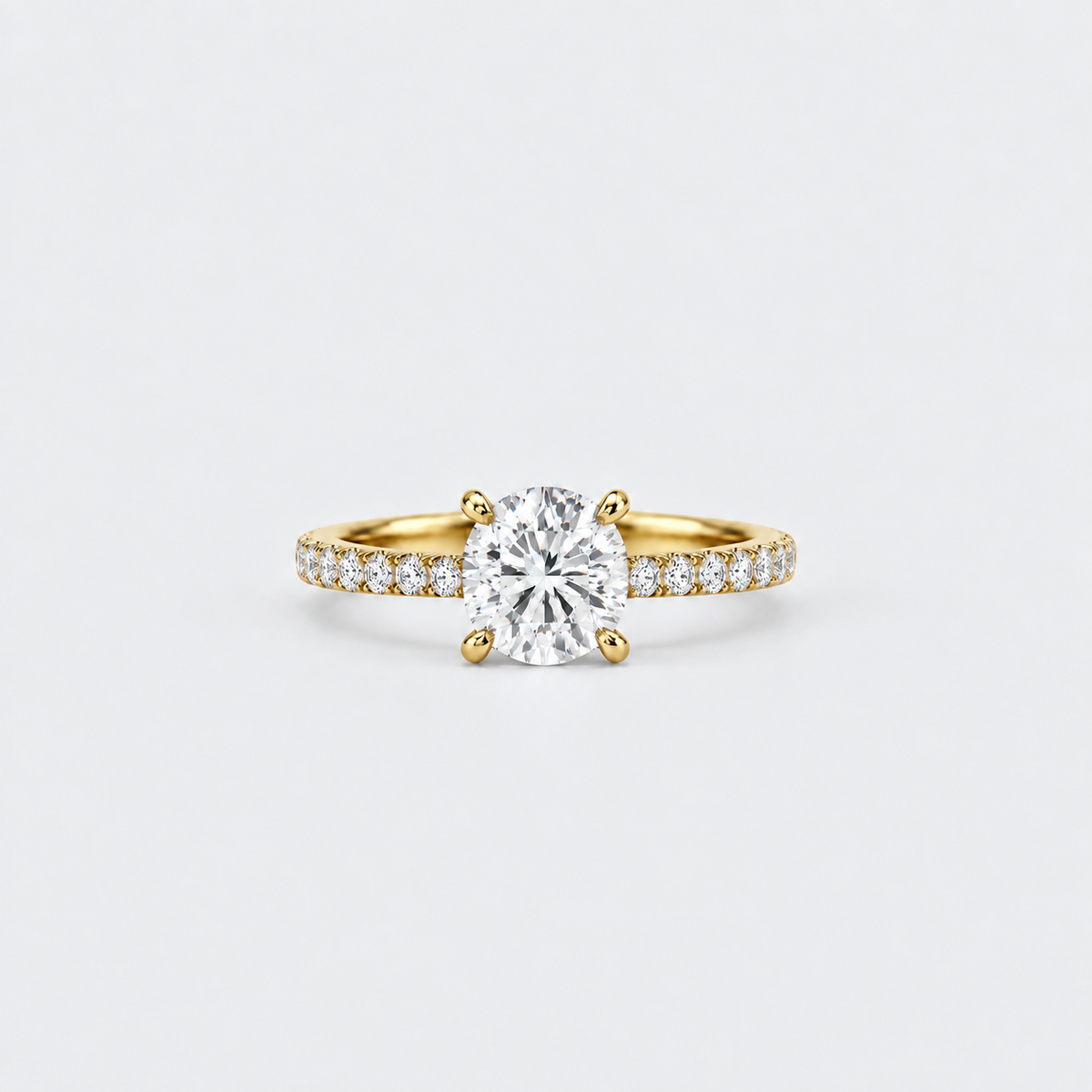 A yellow gold solitaire engagement ring featuring a round brilliant-cut center stone and a pavé-set diamond band, shown on a clean light gray background.