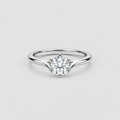 A silver solitaire engagement ring with a round brilliant-cut diamond center stone, set on a plain light gray background.