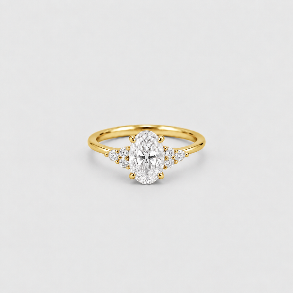 A yellow gold ring featuring an oval-cut center stone and small side stones, photographed on a clean light gray background.