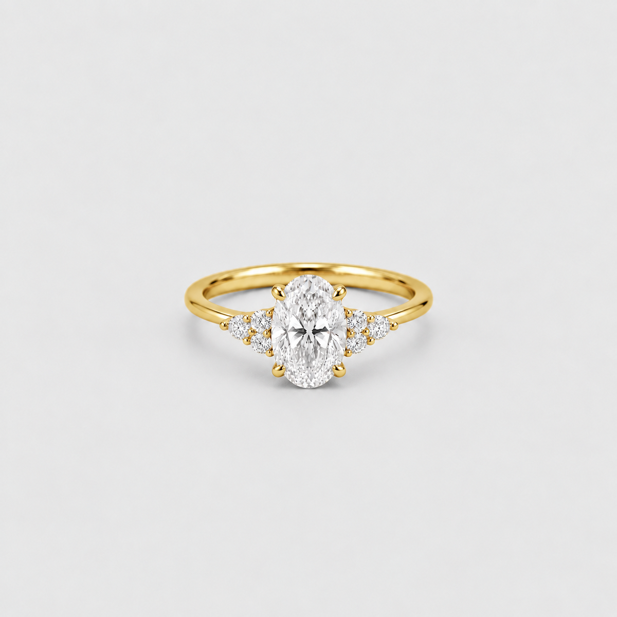 A yellow gold ring featuring an oval-cut center stone and small side stones, photographed on a clean light gray background.