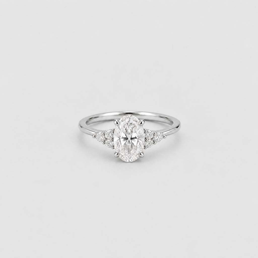 An oval-cut diamond engagement ring with a silver-colored band and small accent diamonds on either side, centered on a light gray background.