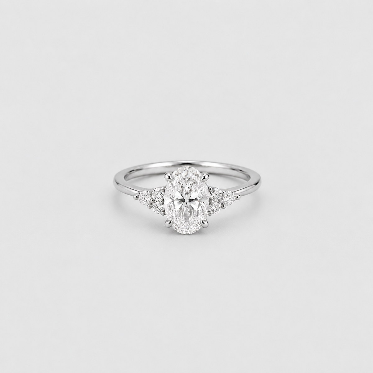 An oval-cut diamond engagement ring with a silver-colored band and small accent diamonds on either side, centered on a light gray background.