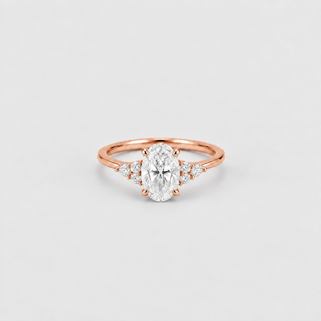 A rose gold engagement ring featuring an oval-cut center stone and small side stones, set on a plain light gray background.