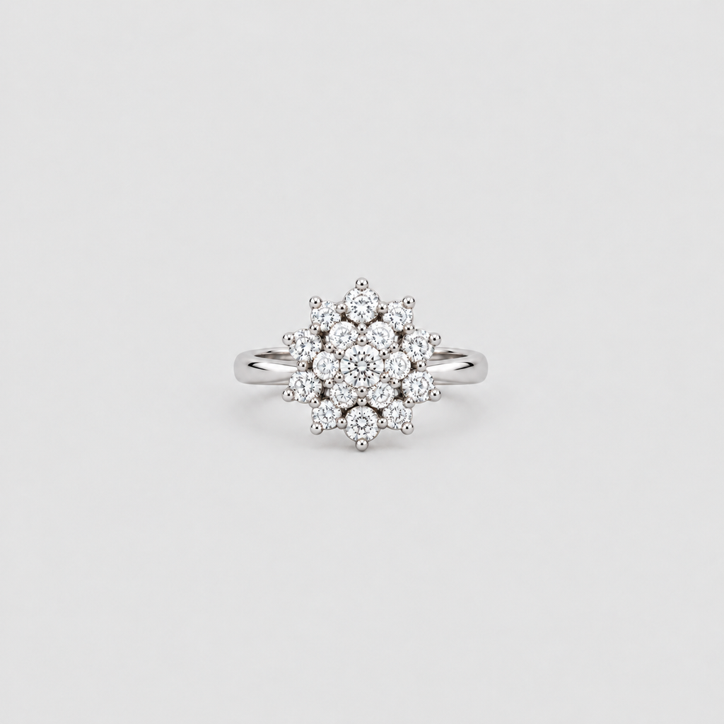 A silver-toned diamond ring with a round cluster of clear gemstones on a plain light gray background.
