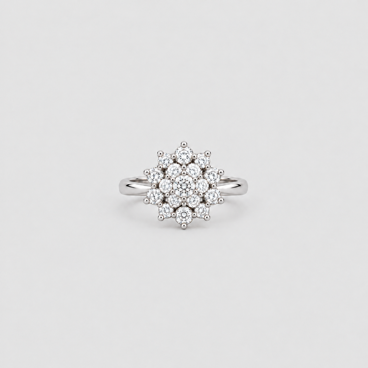 A silver-toned diamond ring with a round cluster of clear gemstones on a plain light gray background.