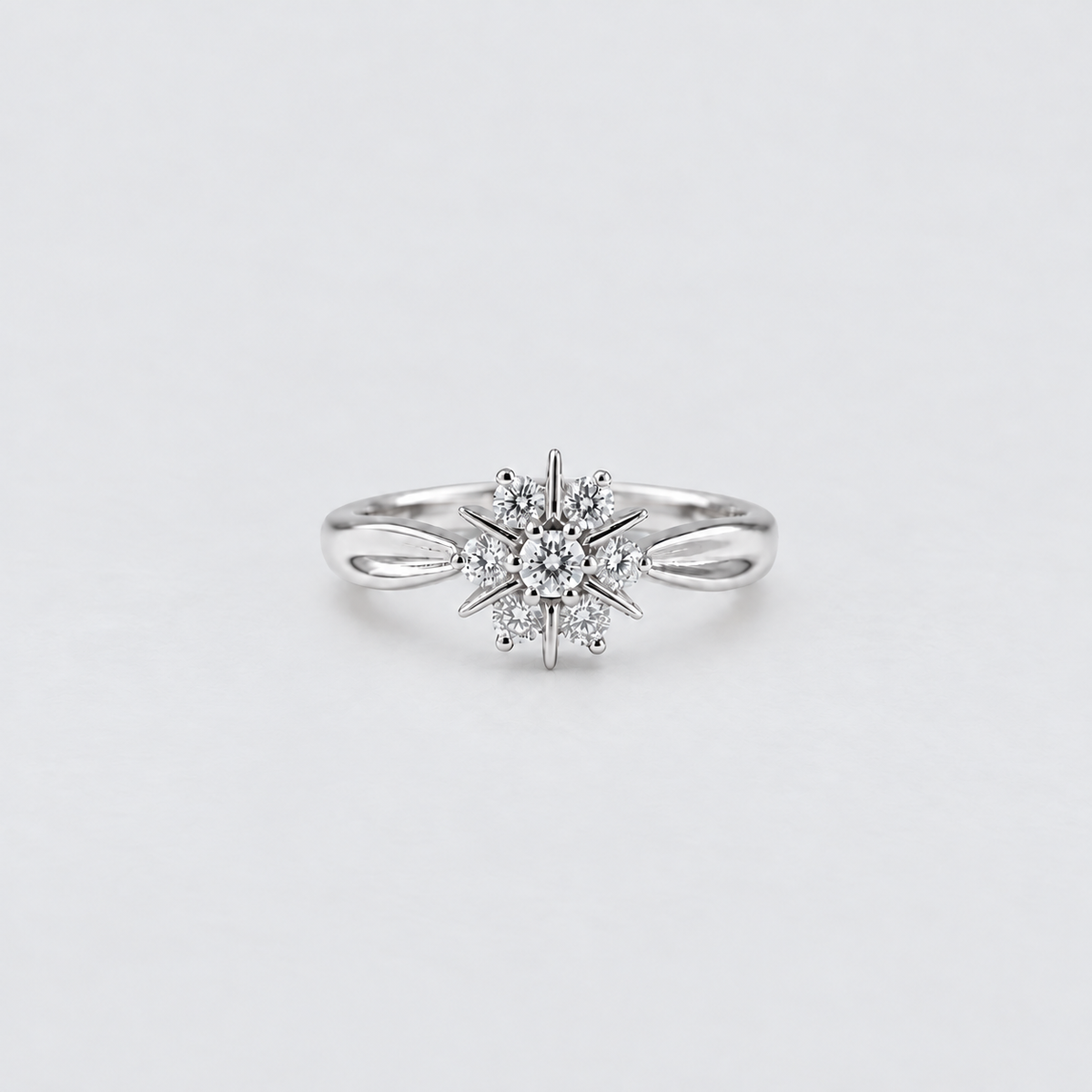 A silver snowflake ring with a central round diamond and smaller surrounding diamonds, set on a plain light gray background.