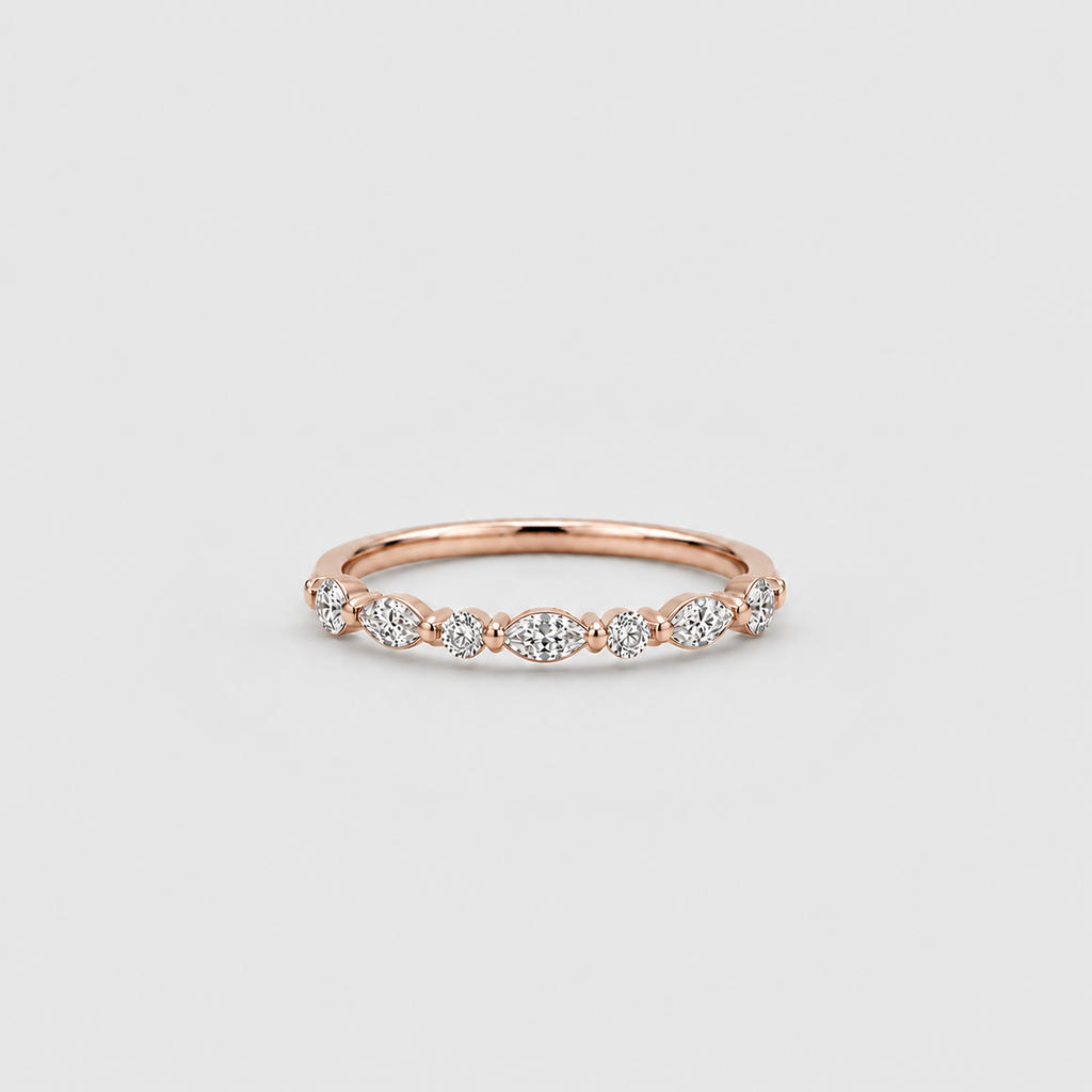 A delicate rose gold eternity ring featuring a row of small round and marquise-cut clear gemstones, photographed on a clean, light gray background.