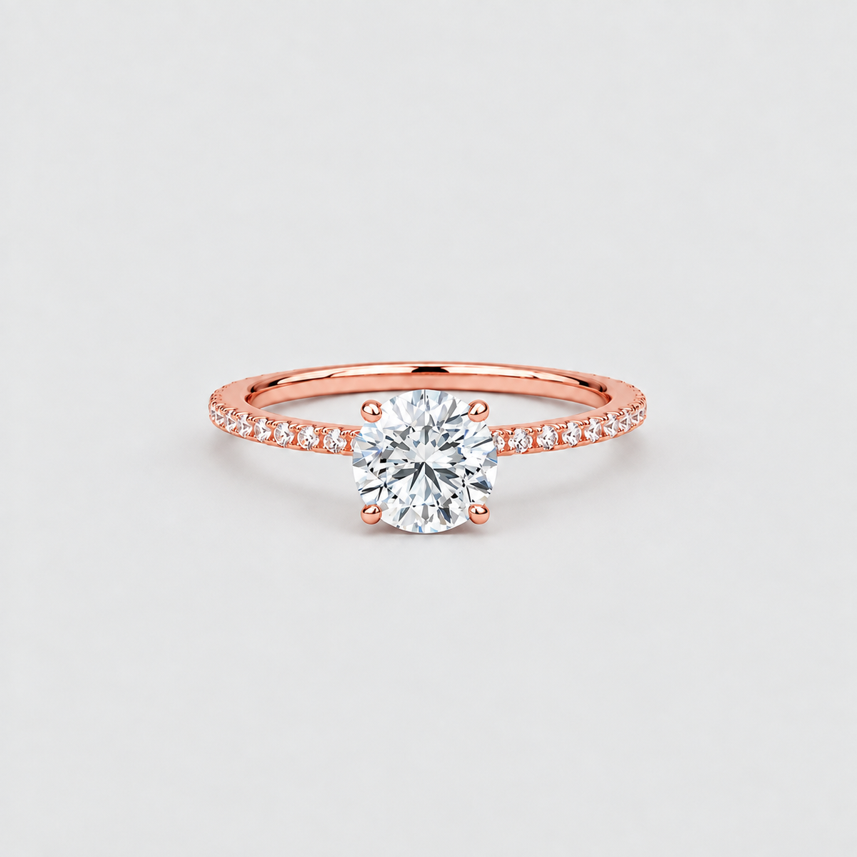 A rose gold solitaire engagement ring with a round brilliant-cut center stone and a pavé-set band, shown on a light gray background.