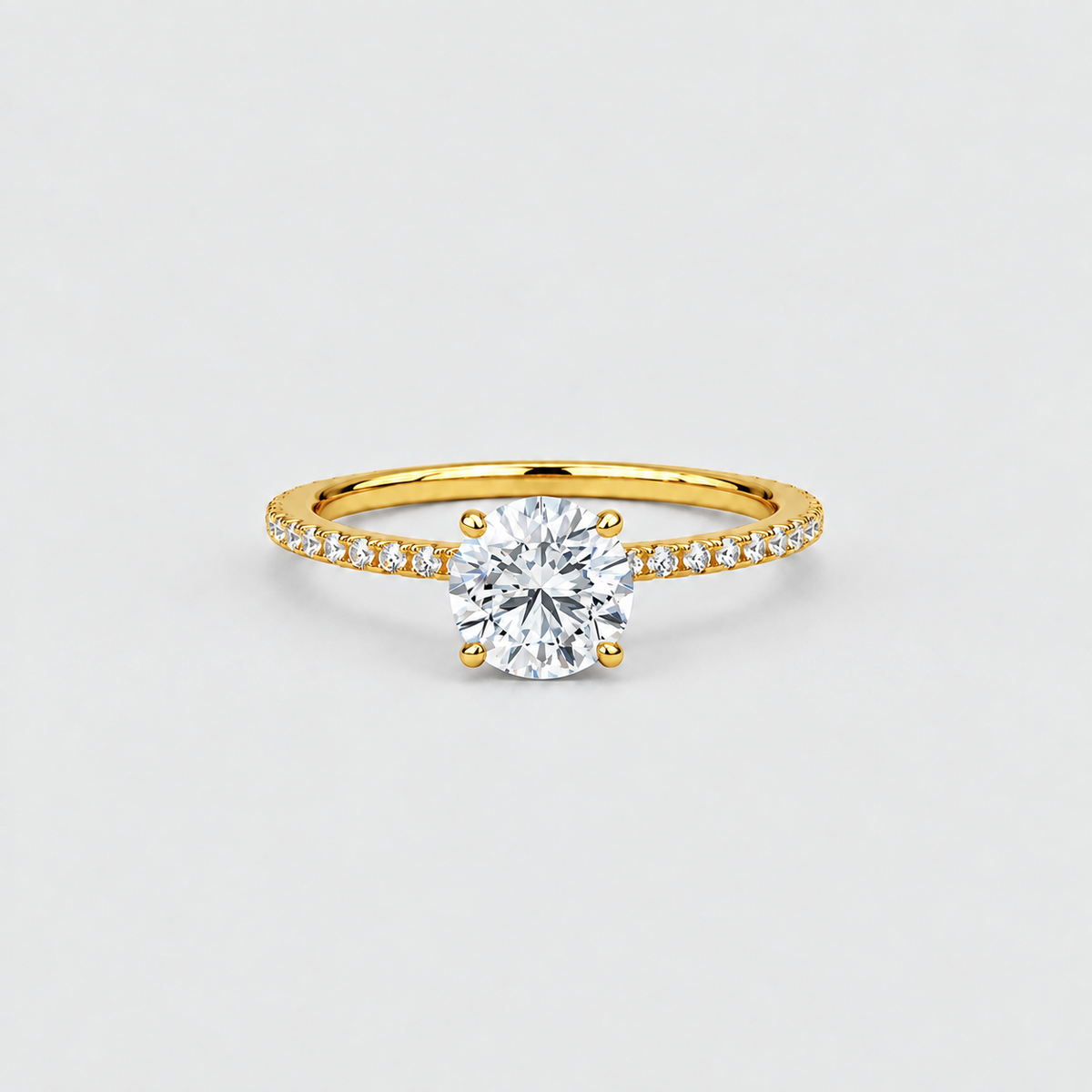 A yellow gold solitaire engagement ring with a round brilliant-cut center stone and a pavé-set diamond band, shown on a light gray background.