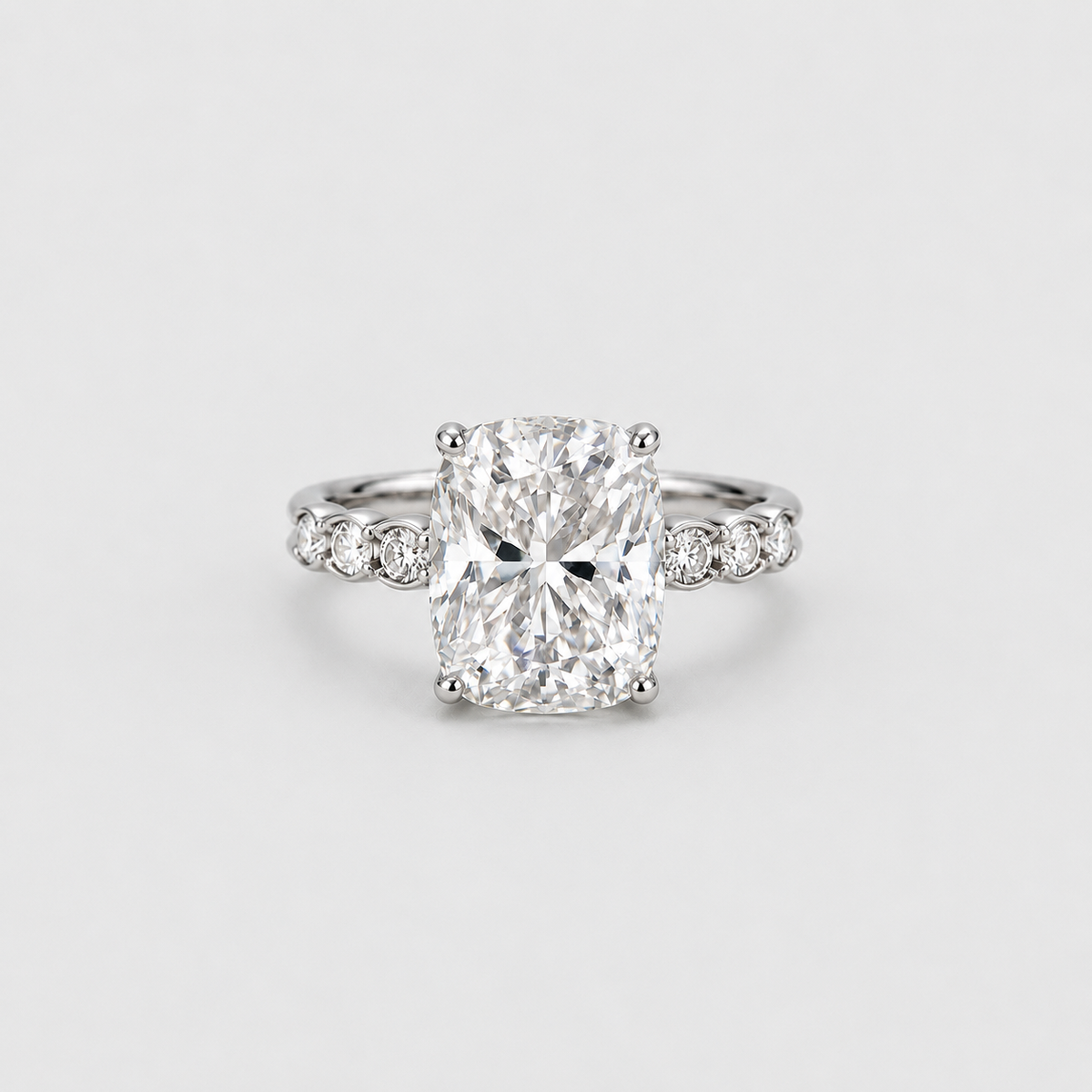 A radiant cut diamond engagement ring with a silver-colored band accented by small side diamonds, centered on a light gray background.