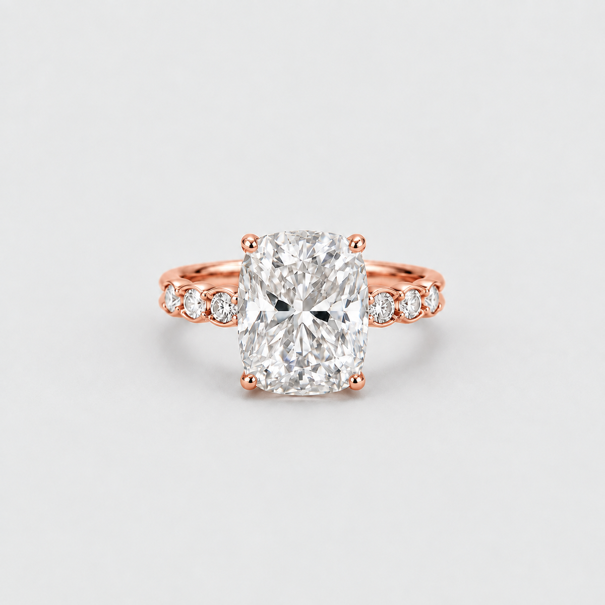 A rose gold engagement ring featuring a large cushion-cut diamond center stone and smaller diamonds set along the band, shown on a light gray background.