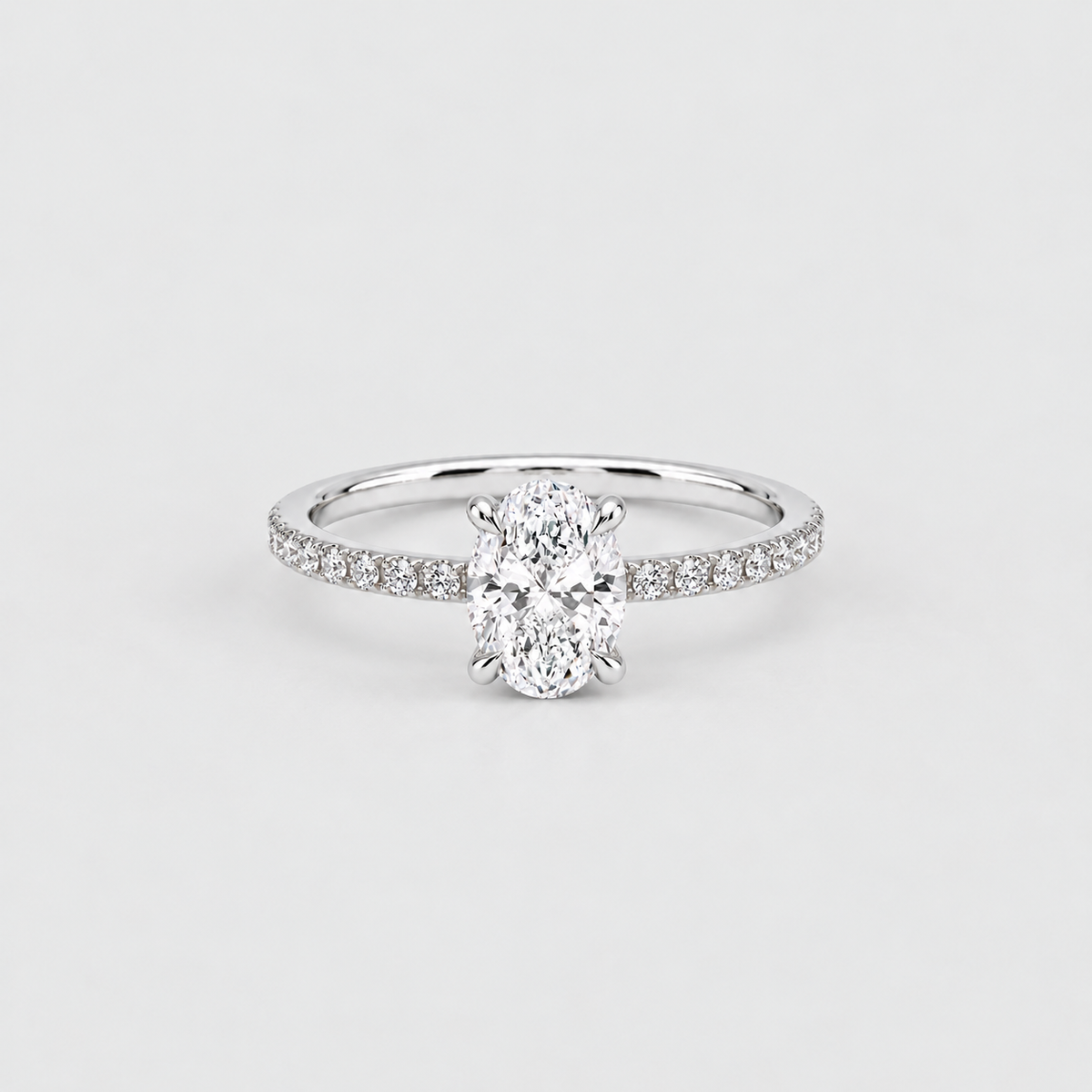 An oval-cut diamond engagement ring with a pavé-set band in white gold or platinum, centered on a light gray background.