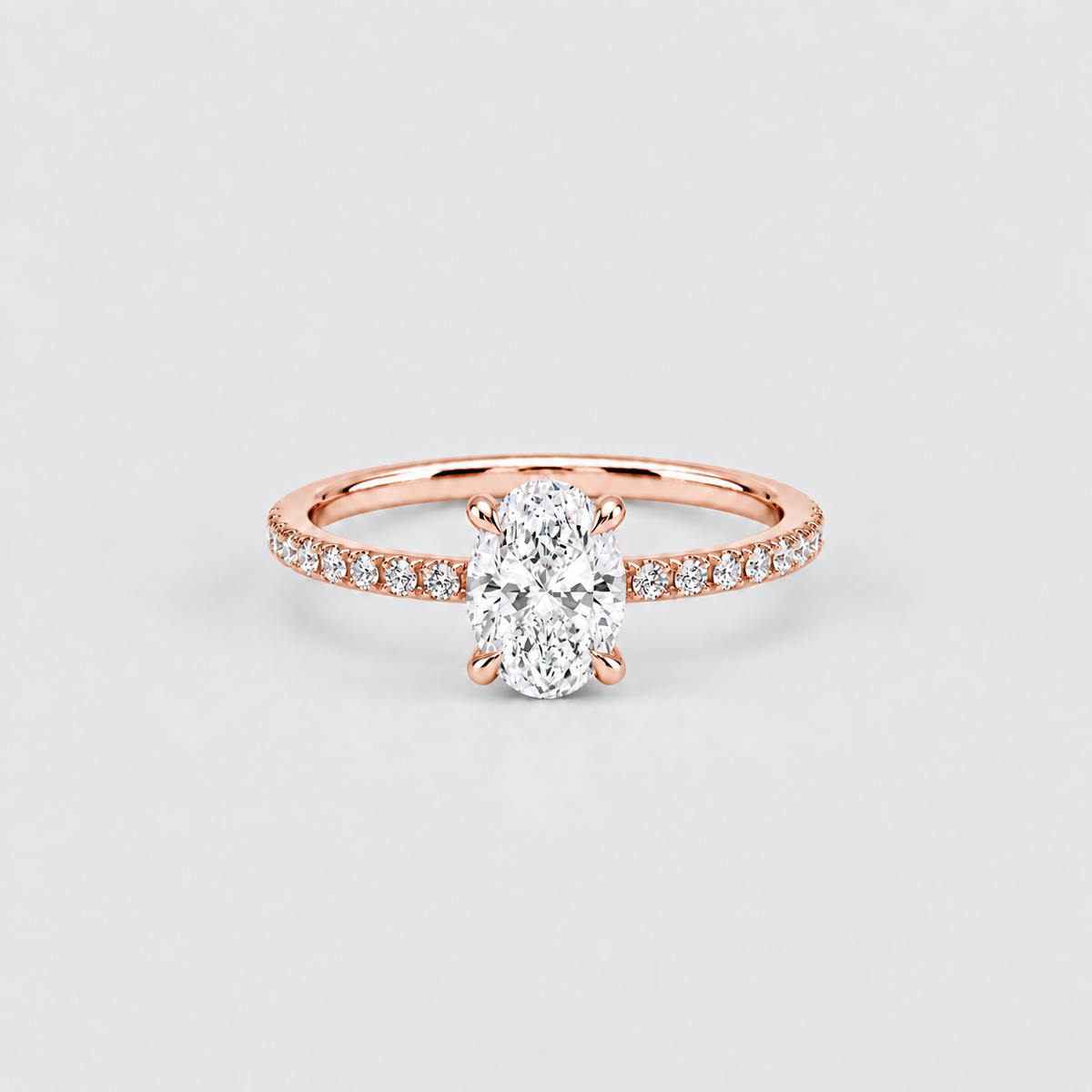 A rose gold engagement ring featuring a large oval-cut center stone and a pavé-set band with small round stones, shown on a light gray background.
