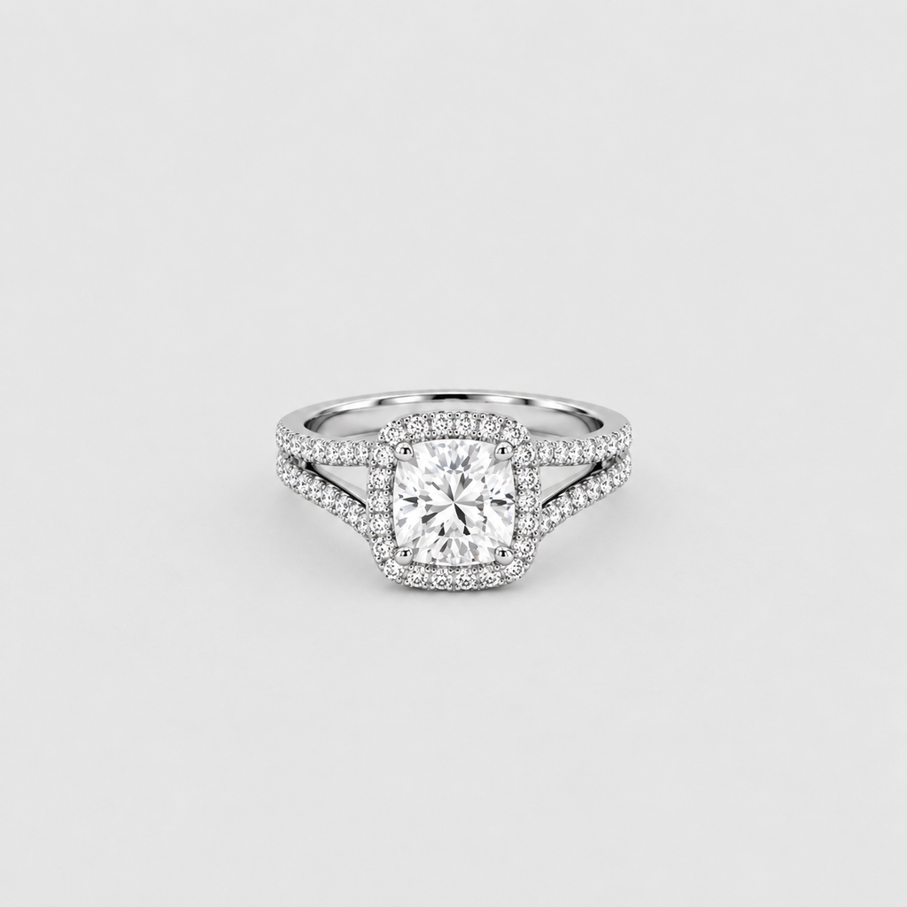 A silver-toned halo ring featuring a cushion-cut center diamond surrounded by a double halo of small round diamonds, with a split shank design, set against a light gray background.