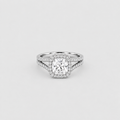 A silver-toned halo ring featuring a cushion-cut center diamond surrounded by a double halo of small round diamonds, with a split shank design, set against a light gray background.