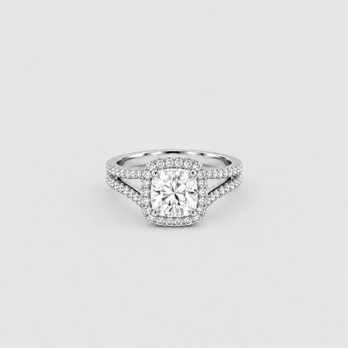 A silver-toned halo ring featuring a cushion-cut center diamond surrounded by a double halo of small round diamonds, with a split shank design, set against a light gray background.