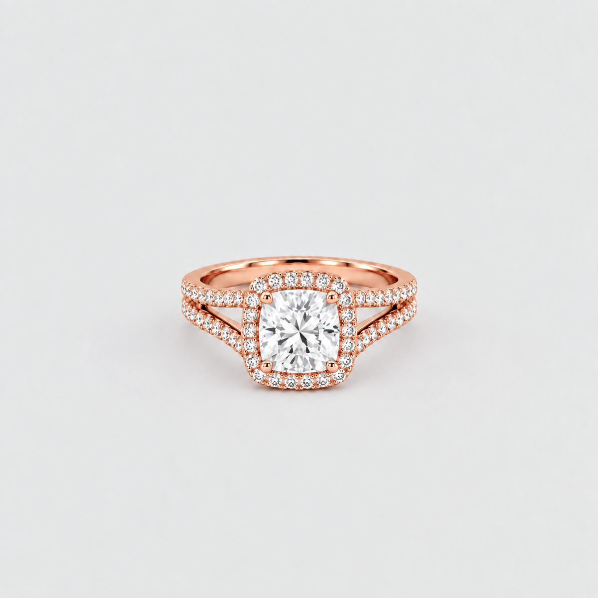 A rose gold engagement ring featuring a cushion-cut center diamond surrounded by a double halo of small pavé diamonds, with a split shank also accented by diamonds, set against a clean light gray background.