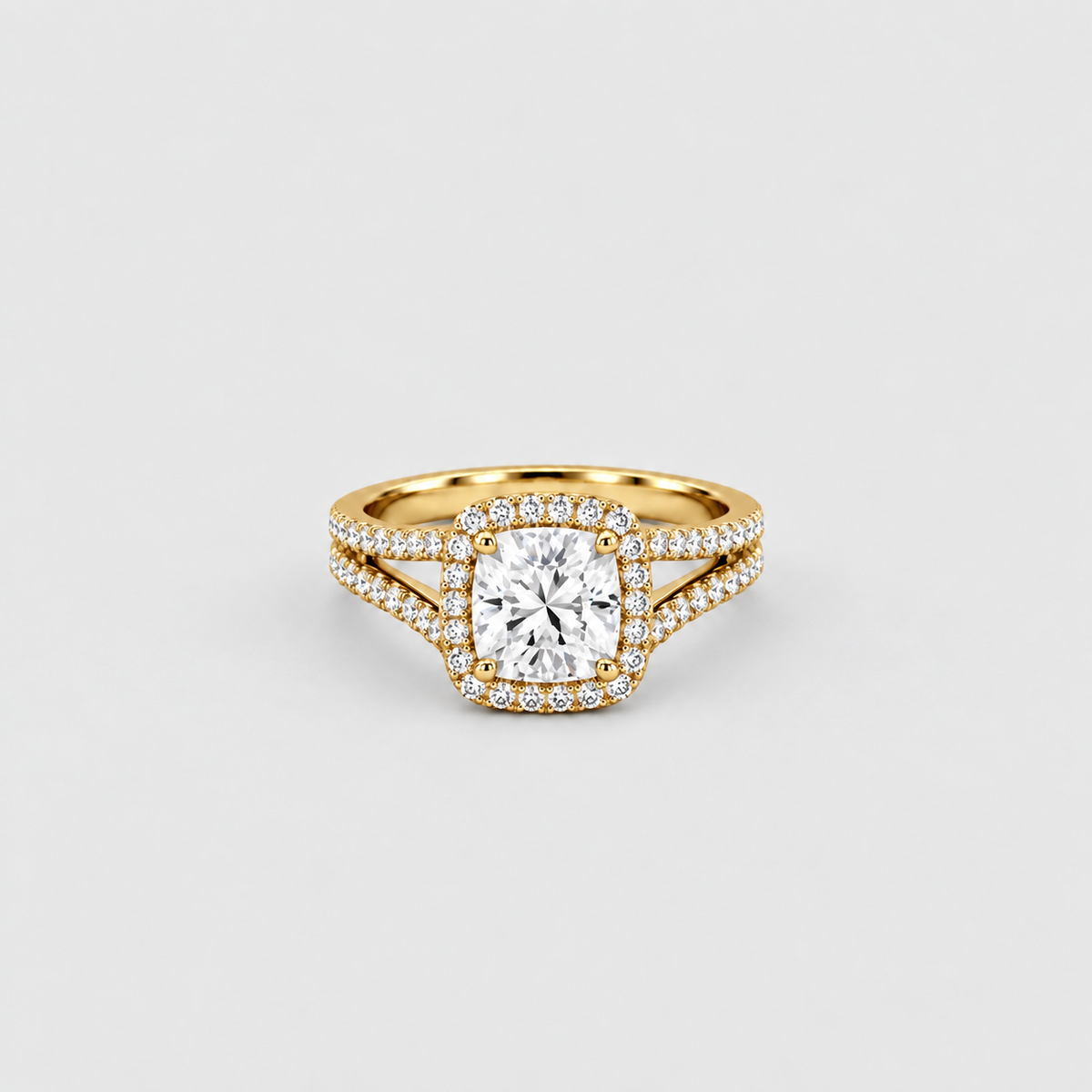 A yellow gold ring featuring a cushion-cut diamond center stone surrounded by a halo of small diamonds, with a split shank also paved with diamonds, set against a clean light gray background.