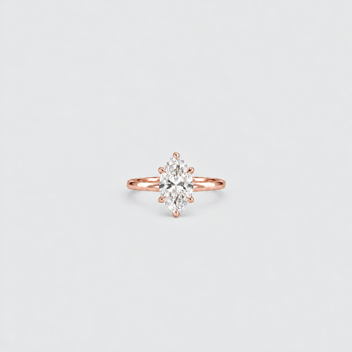 A rose gold ring with a marquise-cut diamond center stone, set against a clean, light gray background.