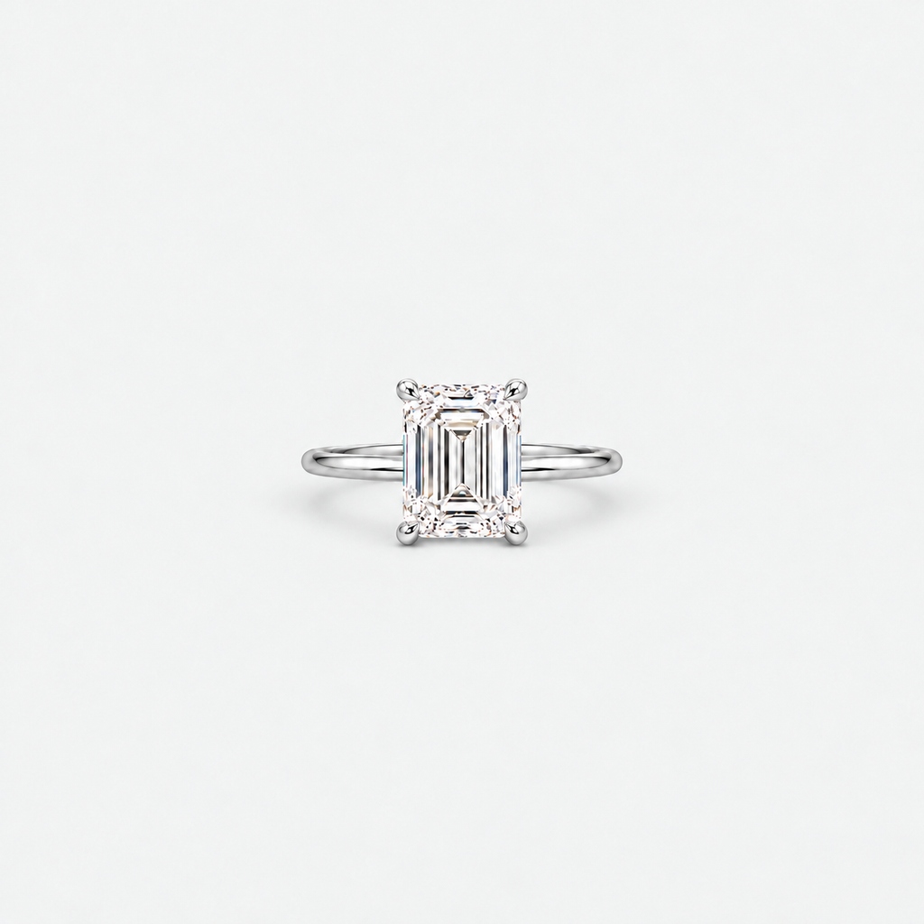 An emerald-cut diamond engagement ring in a silver-toned band, centered on a clean, light gray background.