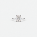 An emerald-cut diamond engagement ring in a silver-toned band, centered on a clean, light gray background.