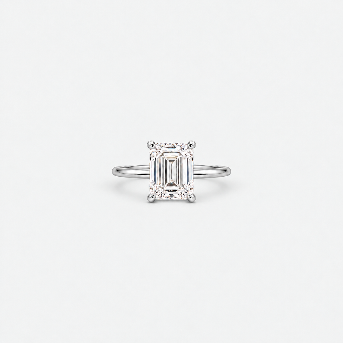An emerald-cut diamond engagement ring in a silver-toned band, centered on a clean, light gray background.