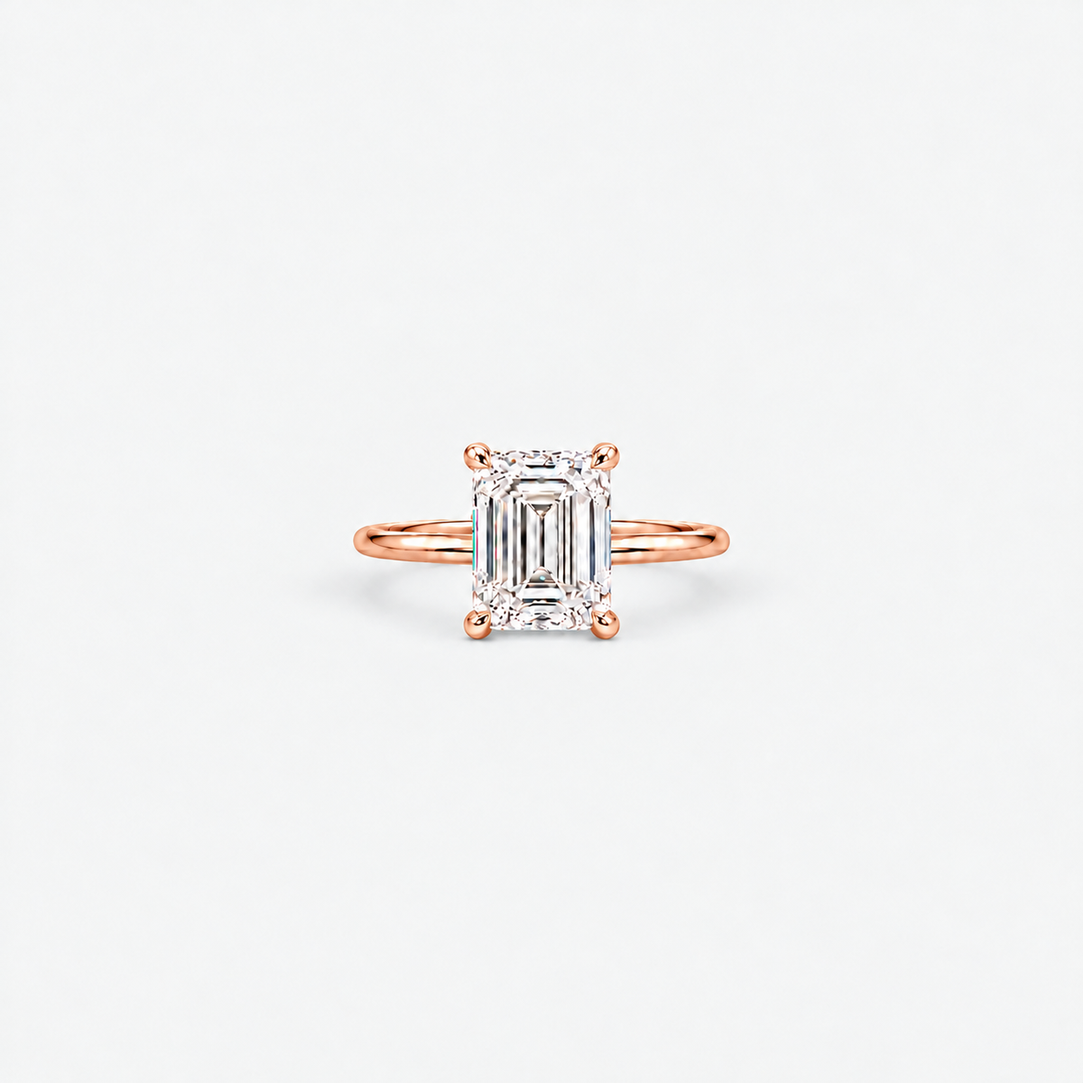 A rose gold engagement ring featuring an emerald-cut diamond center stone in a four-prong setting, shown on a clean white background.