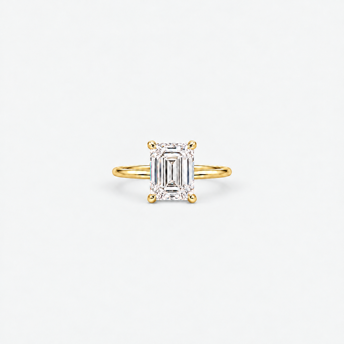 A yellow gold ring featuring an emerald-cut diamond center stone in a four-prong setting, shown against a clean white background.