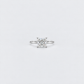 A classic solitaire engagement ring featuring a brilliant round-cut diamond set in a silver-colored metal band, centered on a clean white background.