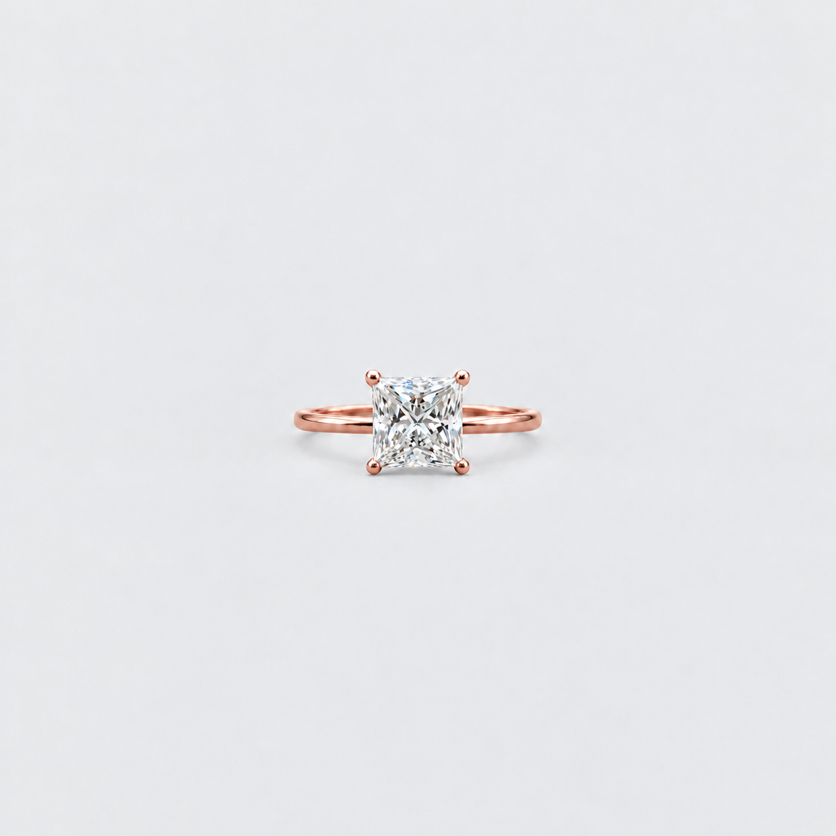 A single-prong rose gold ring with a square radiant-cut clear gemstone, centered on a light gray background.