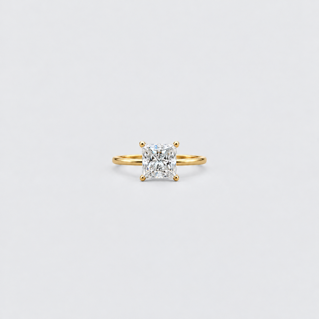 A yellow gold solitaire ring featuring a brilliant cushion-cut diamond in a four-prong setting, centered on a clean, light gray background.