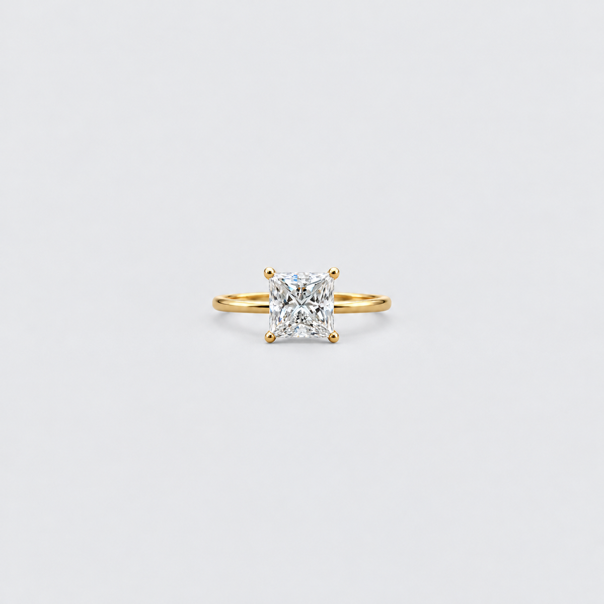 A yellow gold solitaire ring featuring a brilliant cushion-cut diamond in a four-prong setting, centered on a clean, light gray background.