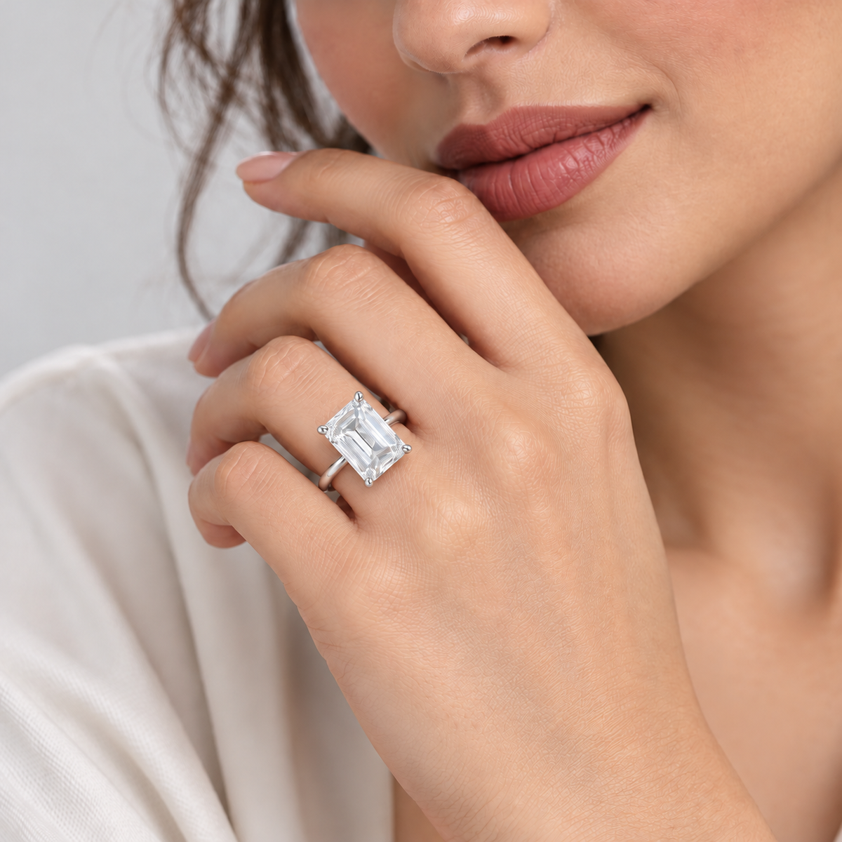 A close-up lifestyle shot of a woman wearing a silver ring with a large rectangular emerald-cut clear gemstone on her finger.