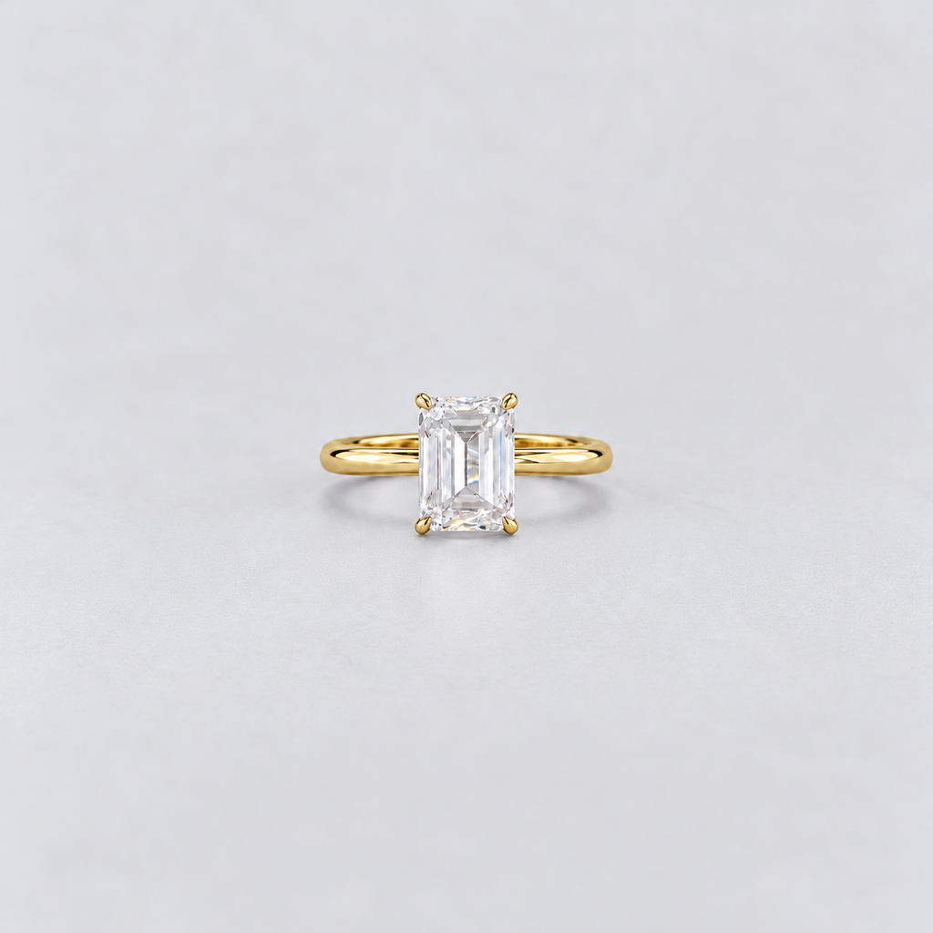 A yellow gold solitaire ring featuring an emerald-cut clear gemstone in a four-prong setting, centered on a light gray background.