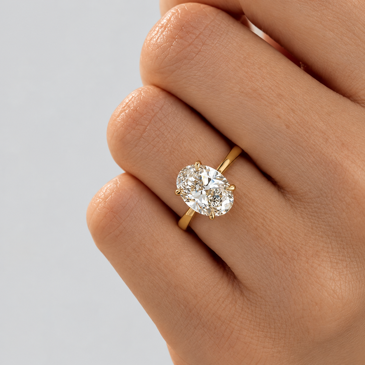 Oval cut diamond solitaire engagement ring in a yellow gold setting worn on a finger.