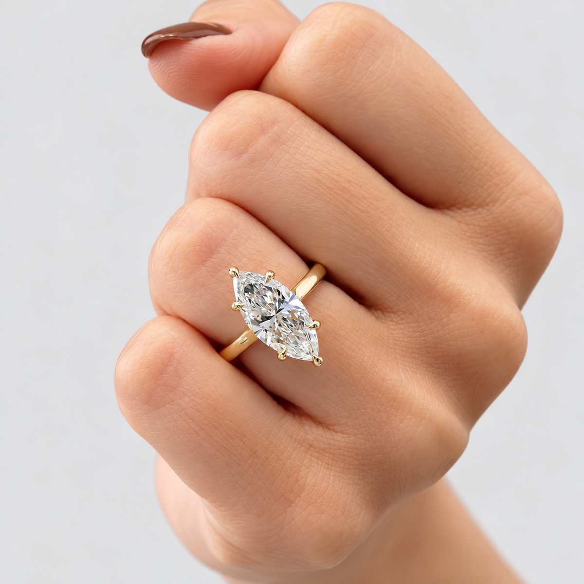 A close-up of a hand wearing a yellow gold ring with a marquise-cut clear gemstone, set against a plain light gray background.