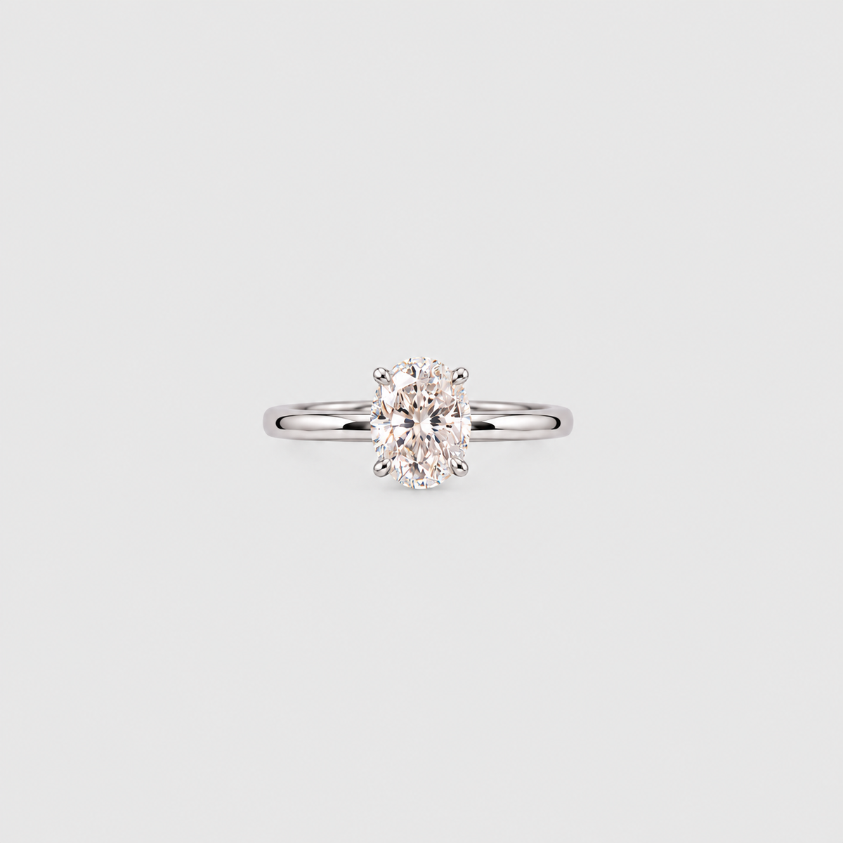 A classic solitaire engagement ring featuring an oval-cut diamond set in a polished white gold or platinum band, centered on a light gray background.