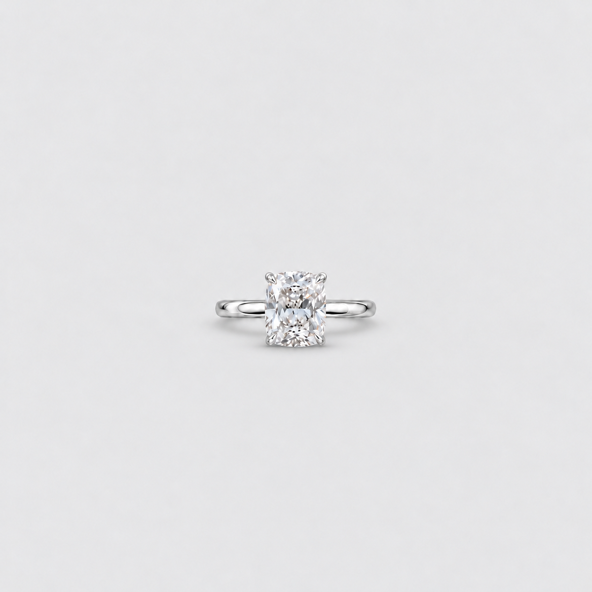 An engagement ring featuring a radiant-cut diamond set in a polished white gold or platinum band, centered on a light gray background.