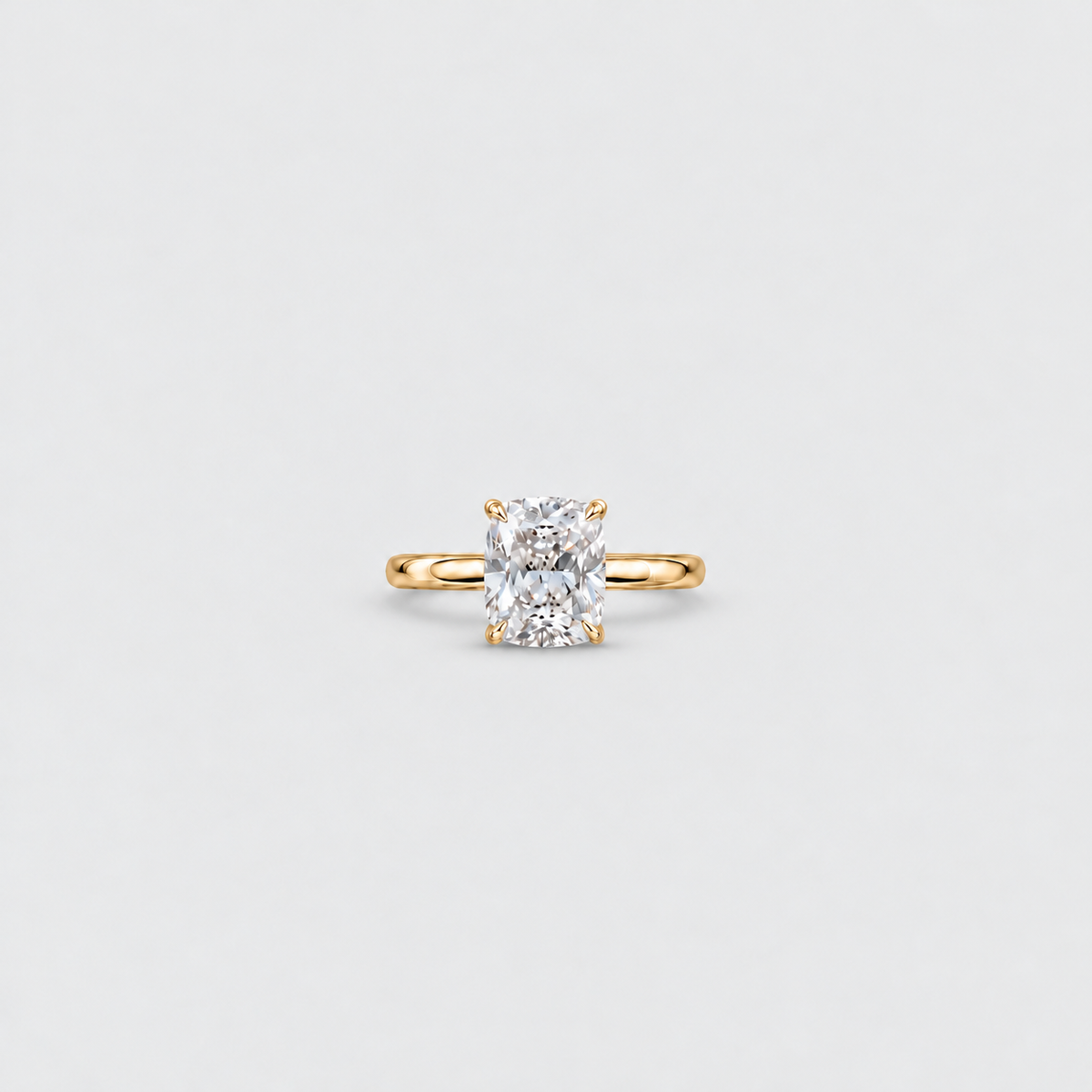 A yellow gold solitaire engagement ring featuring a large cushion-cut diamond, centered on a light gray background.