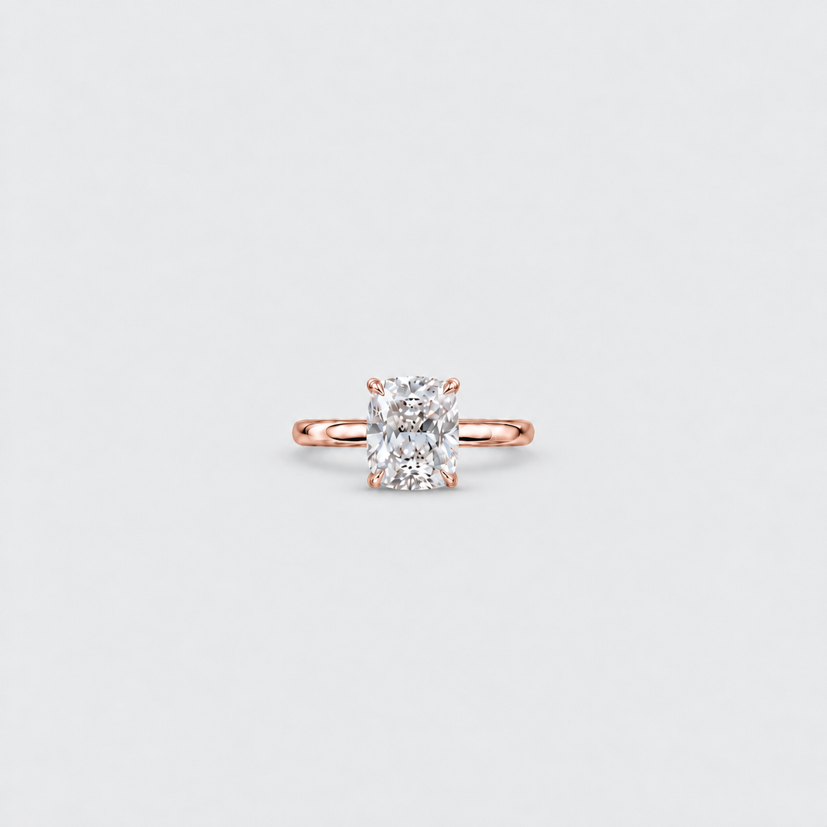 A single solitaire engagement ring featuring a radiant-cut diamond set in a rose gold band, centered on a light gray background.