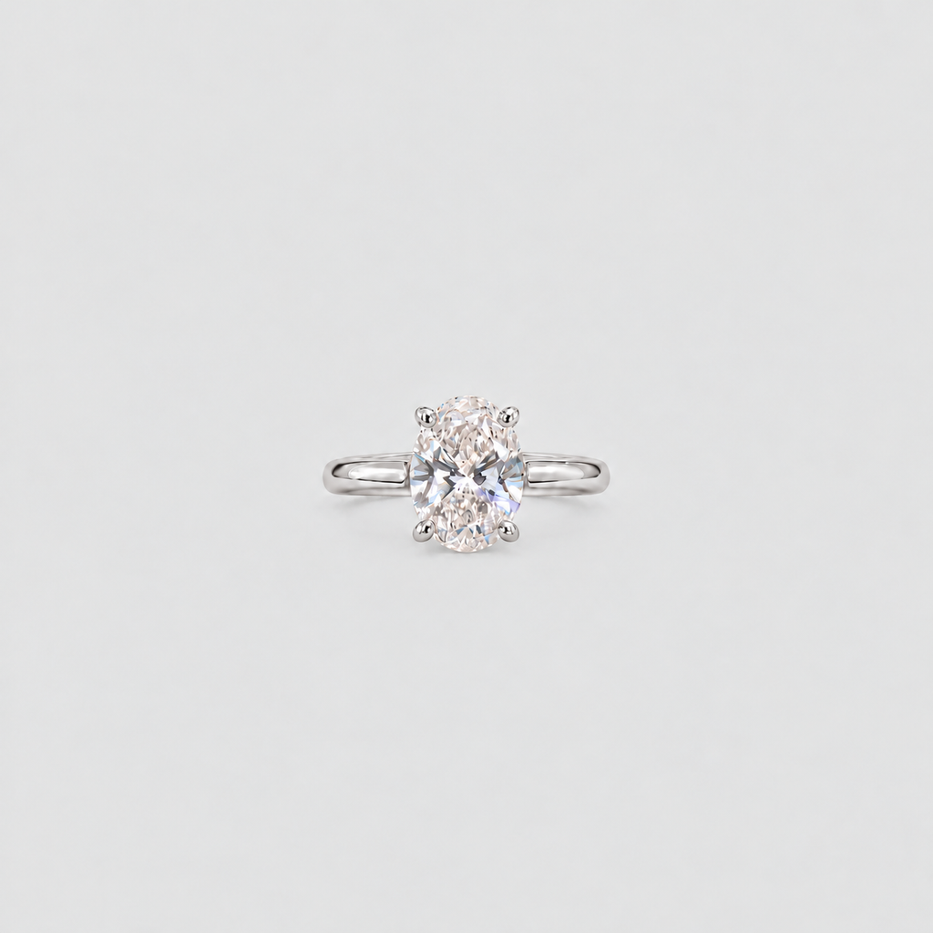 A single solitaire engagement ring featuring a round brilliant-cut diamond set in a polished silver-colored band, centered on a light gray background.